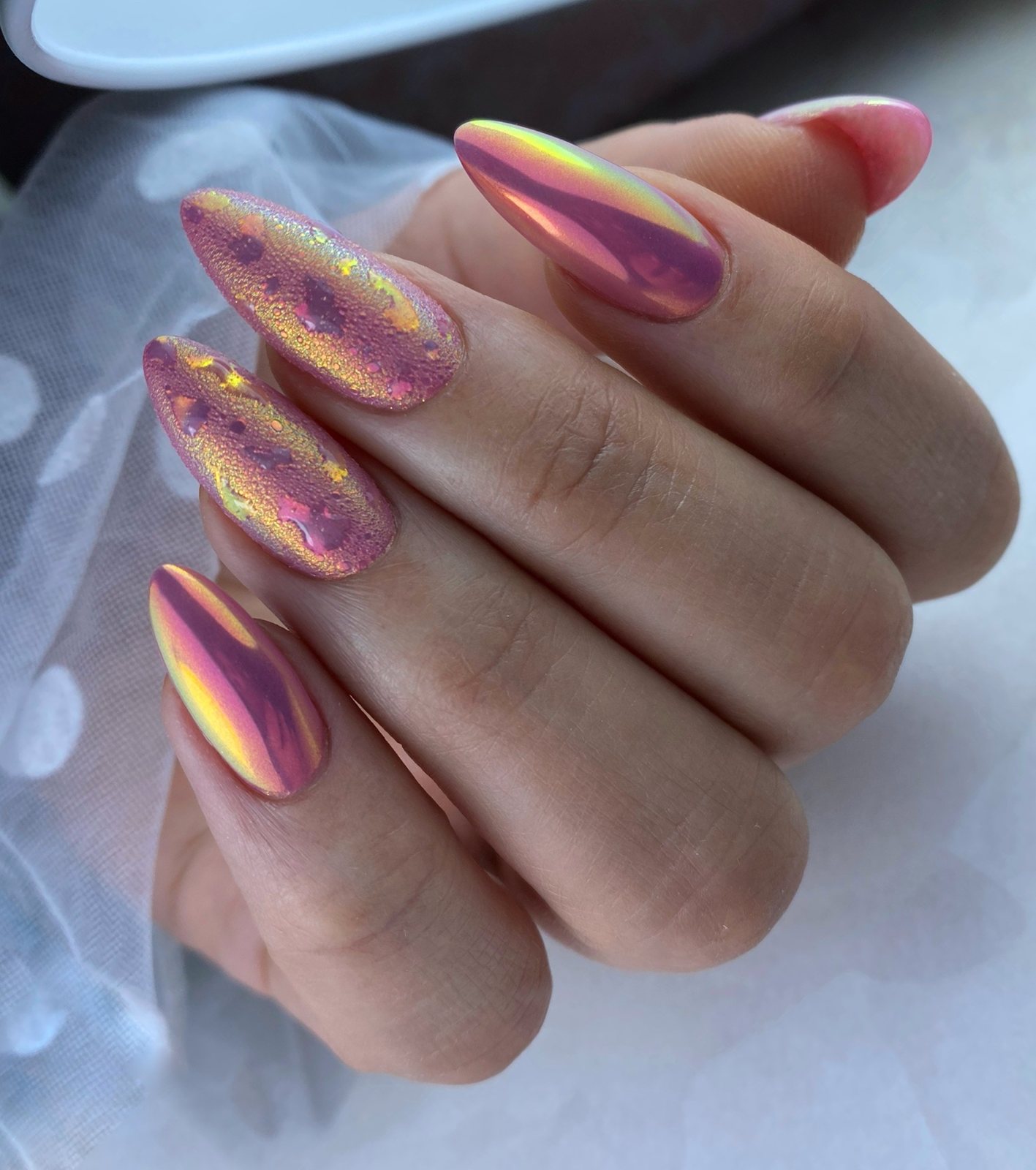 Roze-gouden chrome nagels in amandelvorm op een hand