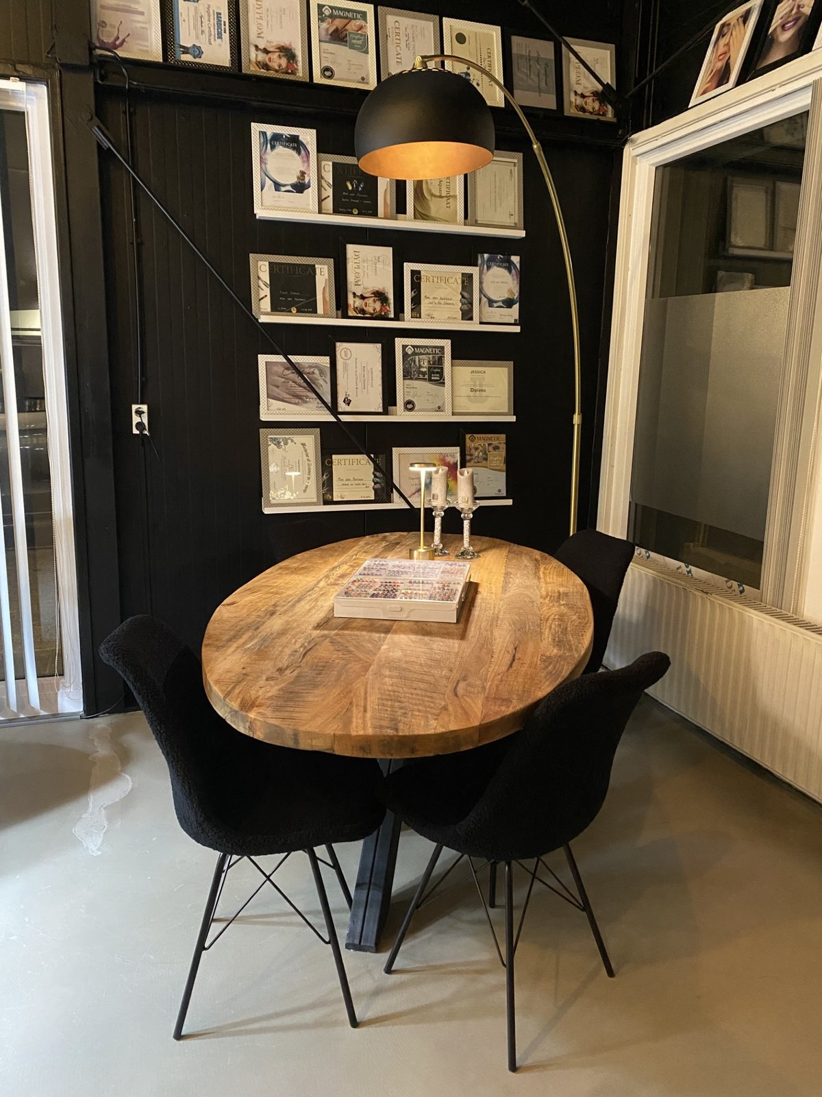 Ronde houten tafel met zwarte stoelen voor een donkere wand met ingelijste certificaten