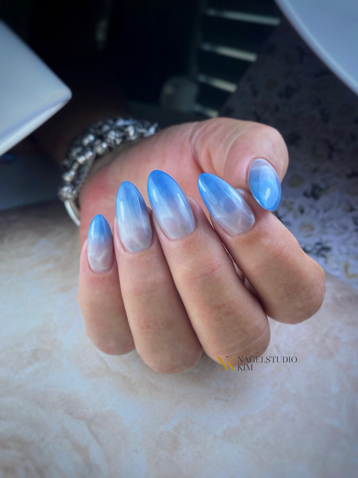 Blauwe ombre nagels op een hand met een armband
